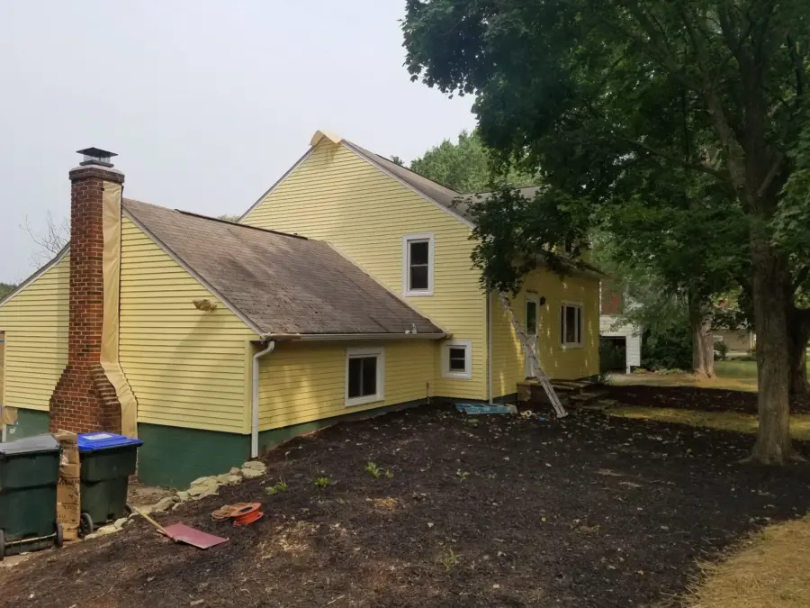 A yellow house with a brick chimney is sitting on top of a dirt hill.