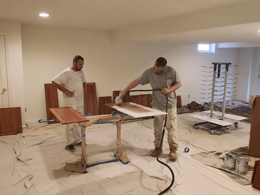 Two men are painting a piece of wood in a room.