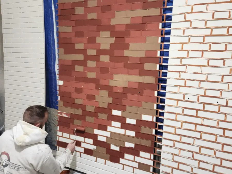 A man is kneeling down in front of a brick wall.