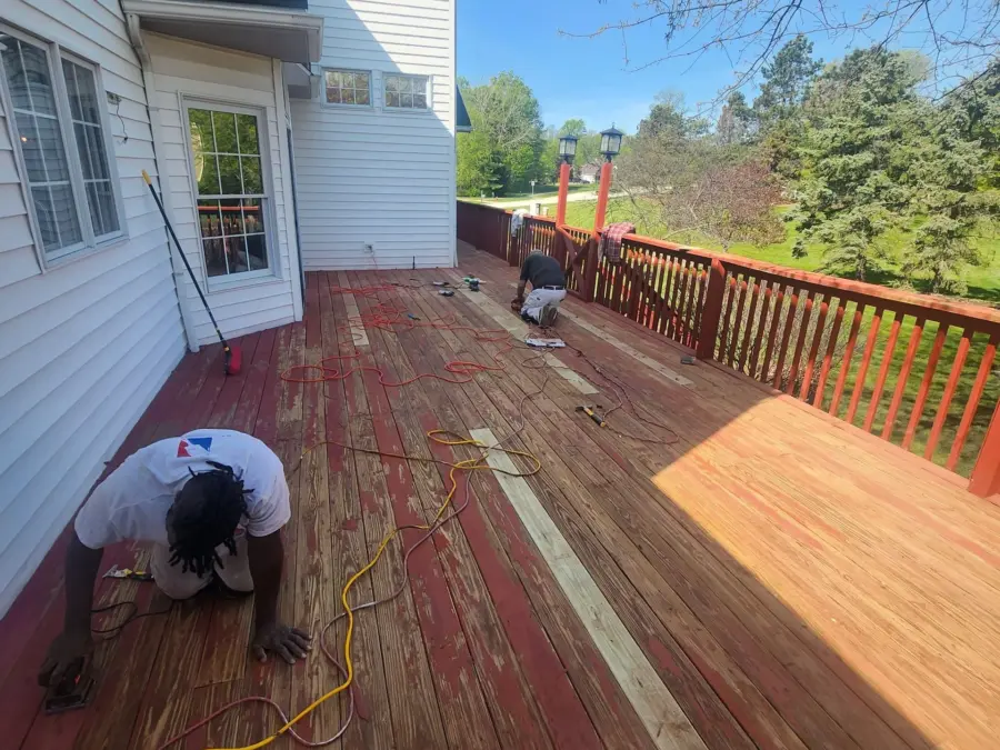 A man is kneeling on a wooden deck next to a house.