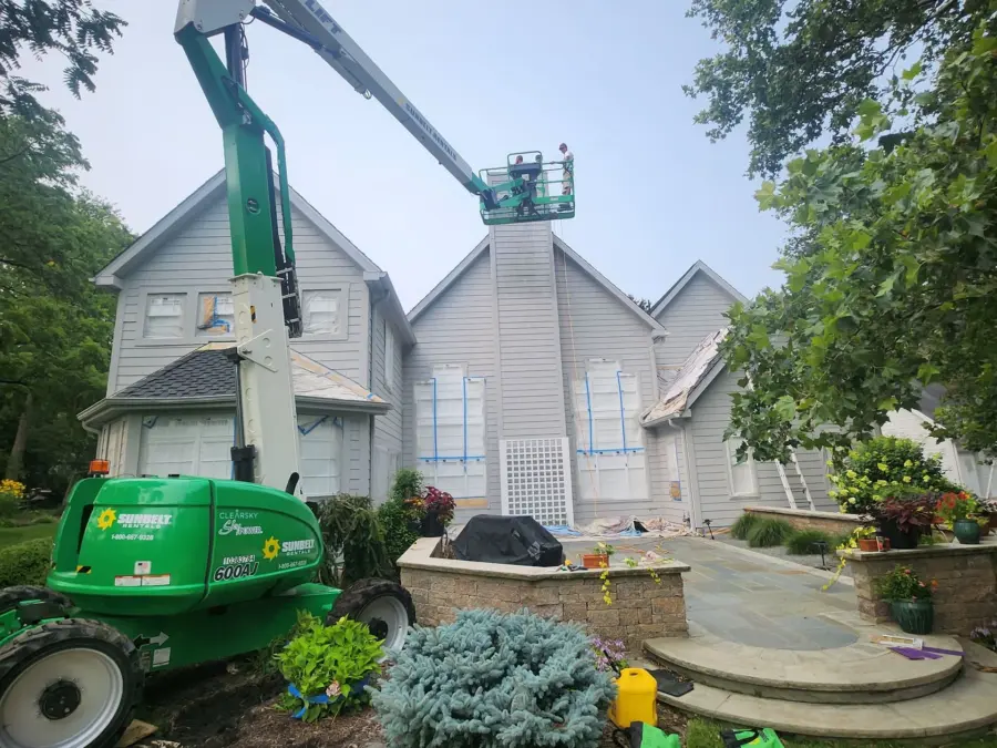 A green crane is sitting in front of a house.