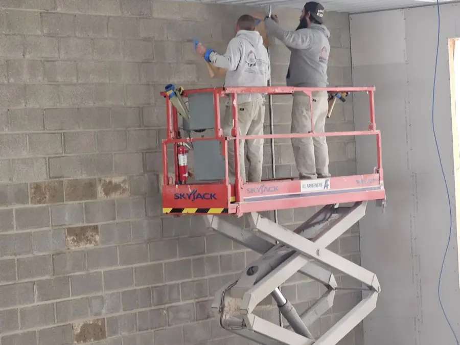 Two men are standing on a scissor lift working on a brick wall.