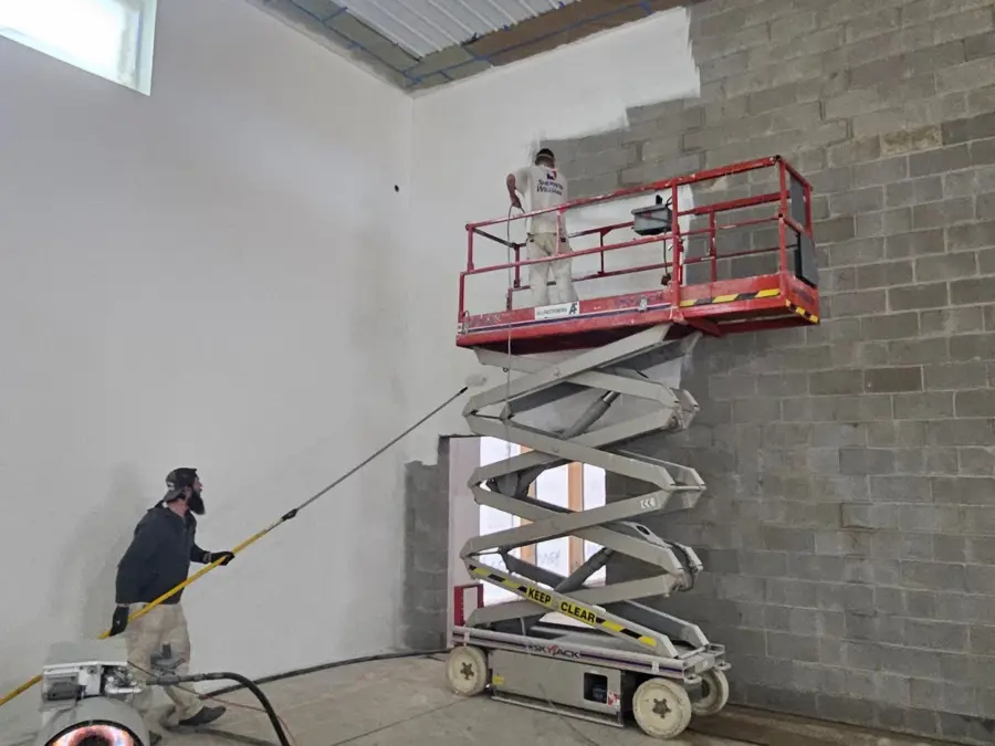 A man is standing on a scissor lift painting a wall.