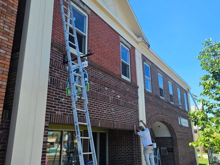 A man on a ladder is painting a brick building
