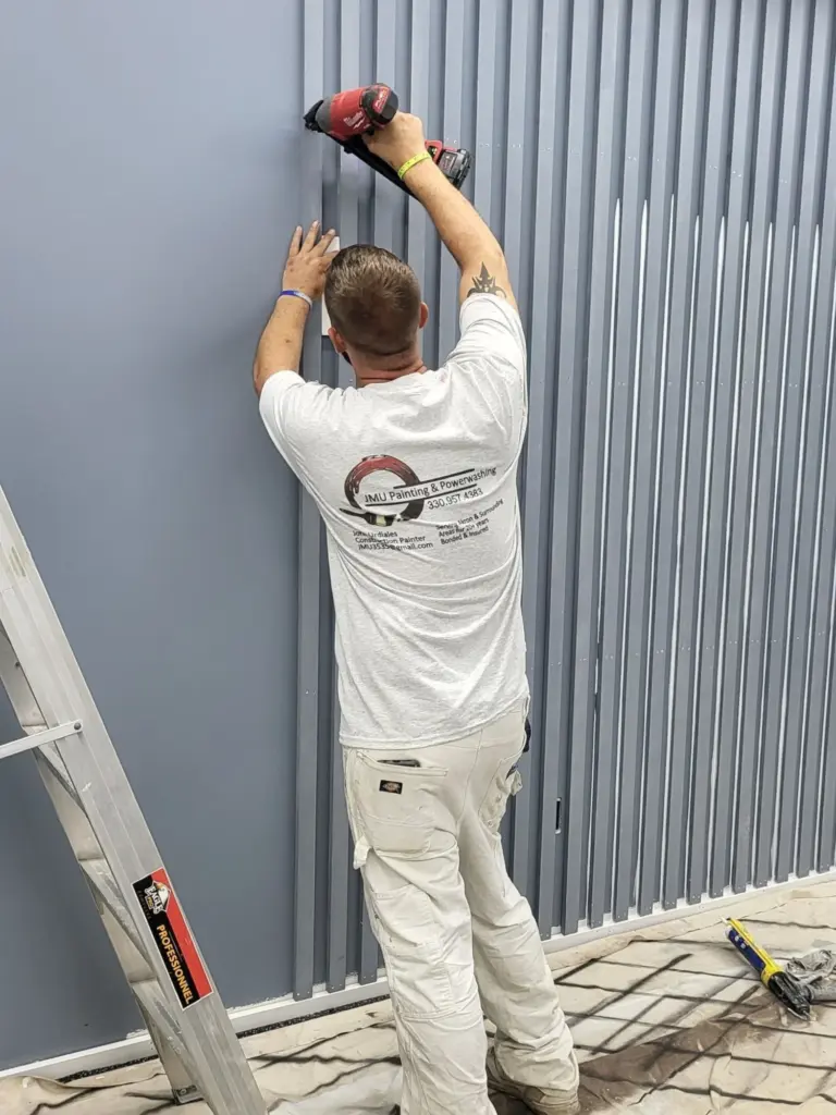 A JMU Painting crew member in branded company whites fastening trim on a job site in Summit County, Ohio