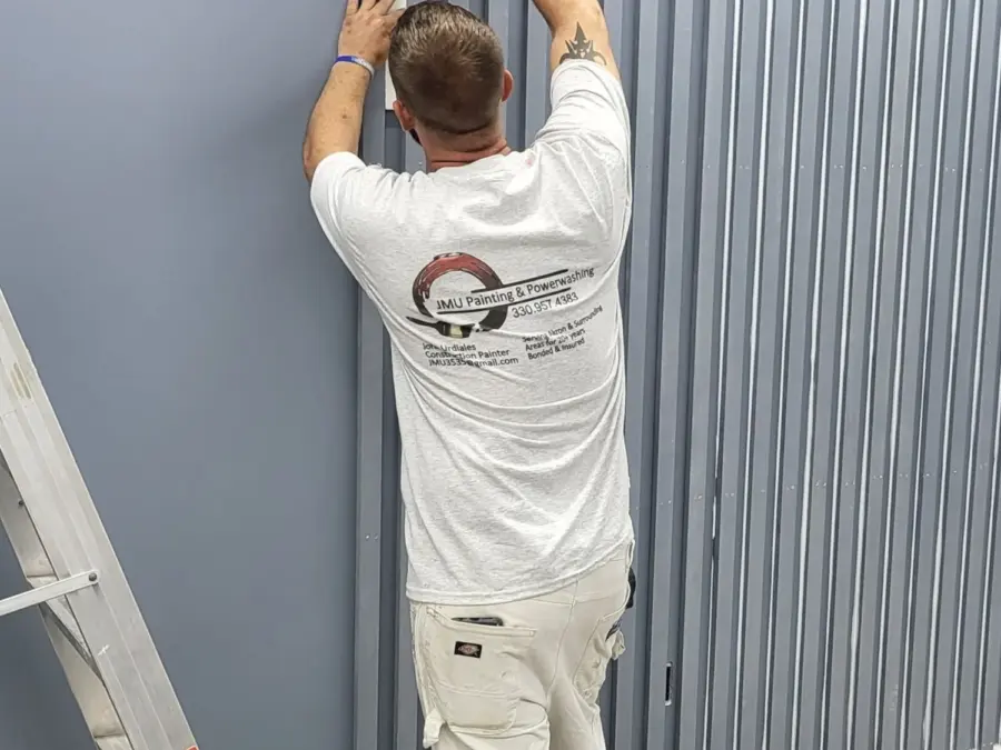 A JMU Painting crew member in branded company whites fastening trim on a job site in Summit County, Ohio