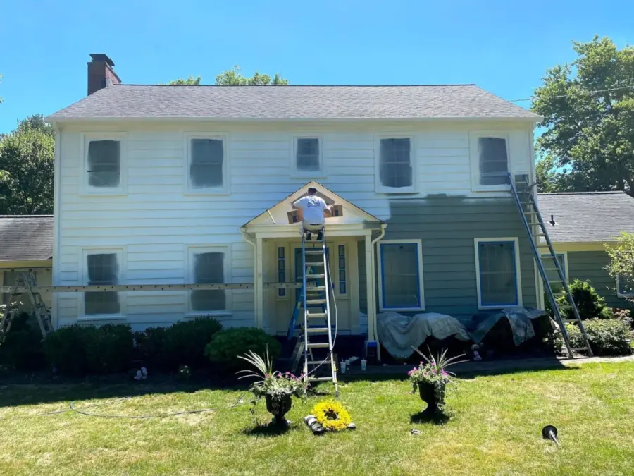A man is standing on a ladder painting the side of a house.