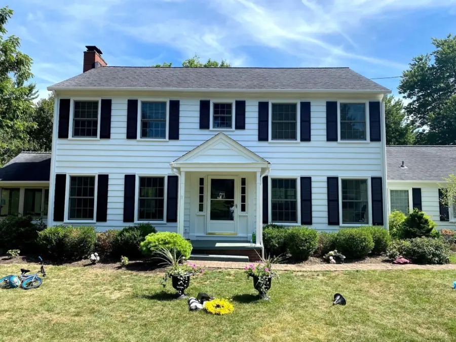 A large white house with black shutters is sitting on top of a lush green lawn.