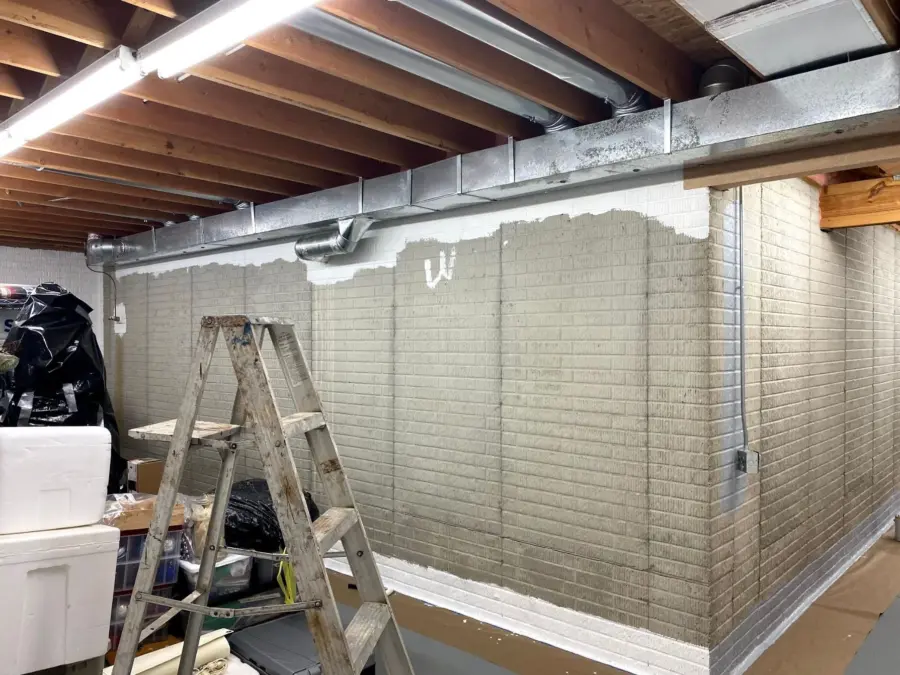 A ladder is sitting in a basement next to a brick wall.
