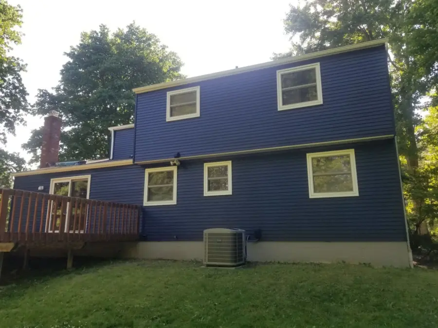 The back of a blue house with a deck and air conditioner.