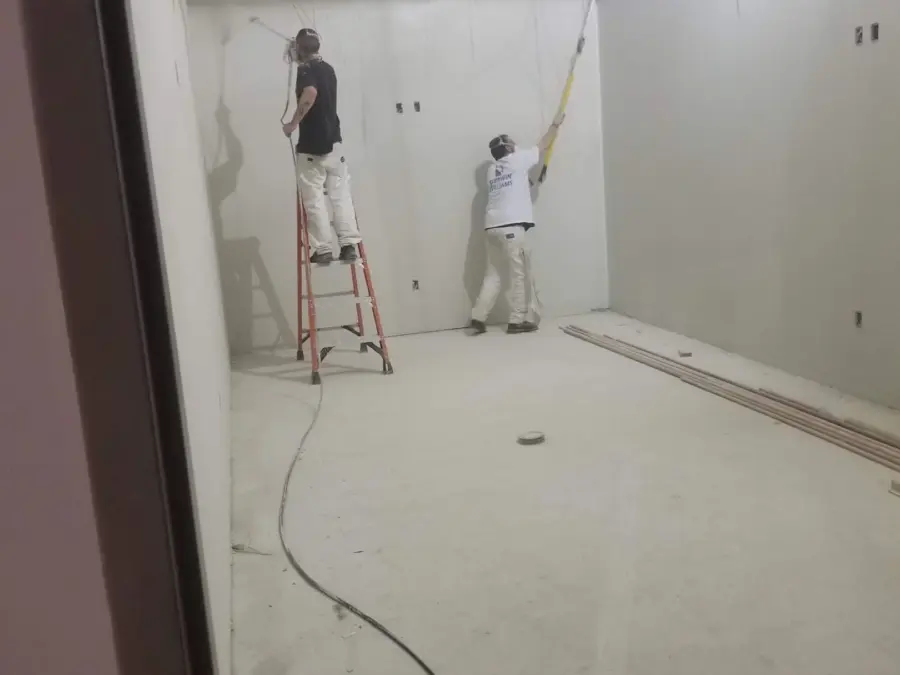 Two men are painting a wall in a room.