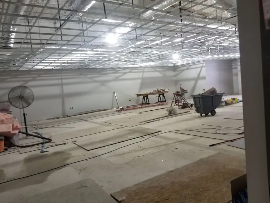 A large empty room with a fan and a trash can in it.