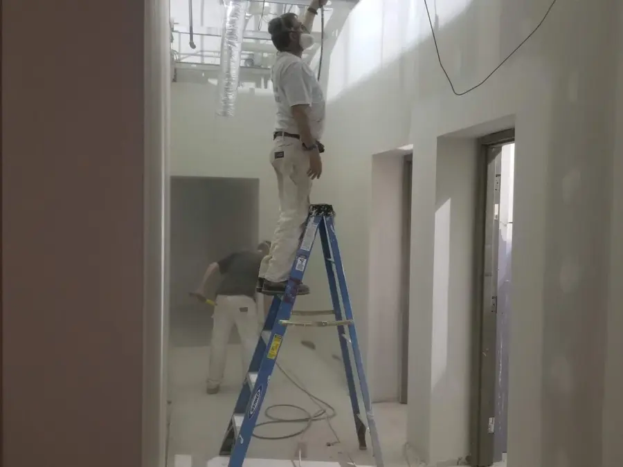 A man is standing on a ladder painting a wall.