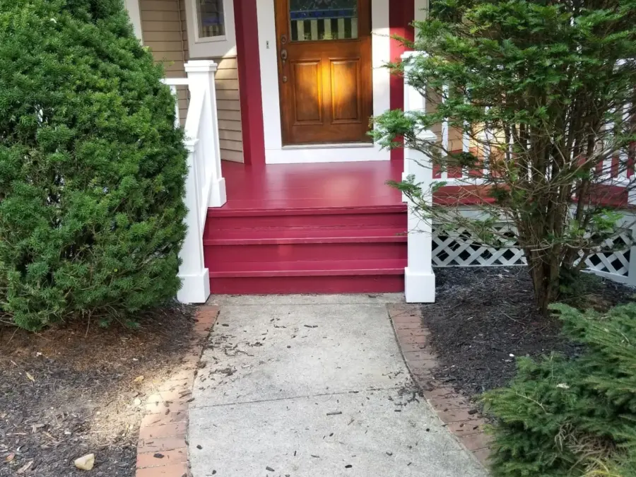 The front porch of a house with red steps and a walkway leading to it.