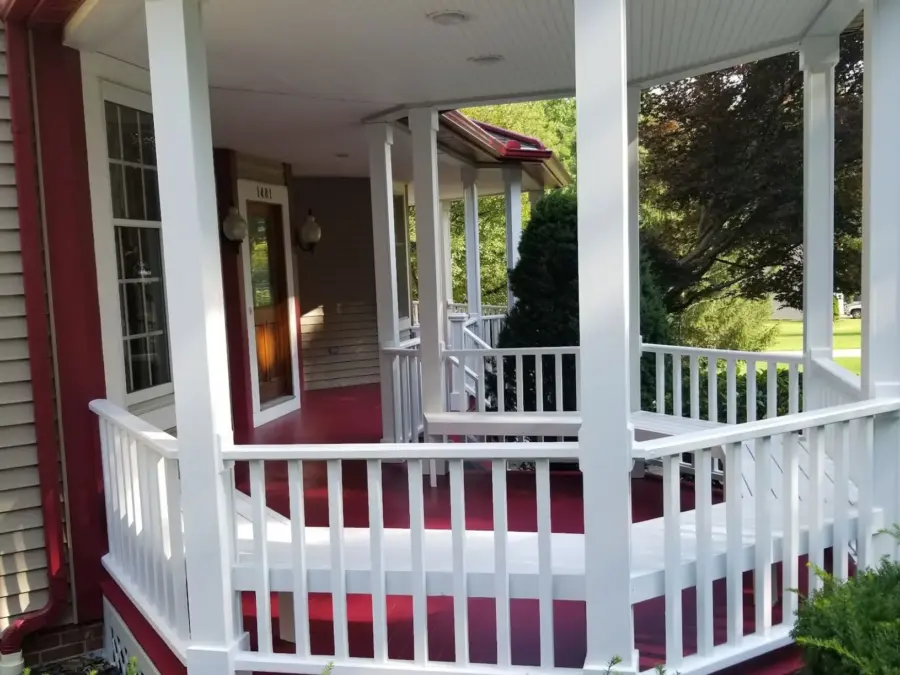 A porch with a white railing and a red rug