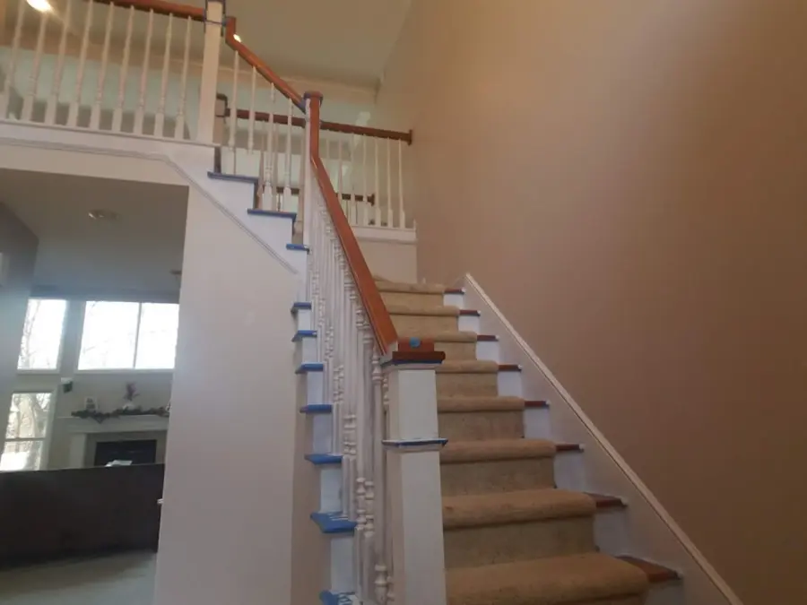 A staircase in a house with a carpeted staircase and a wooden railing.